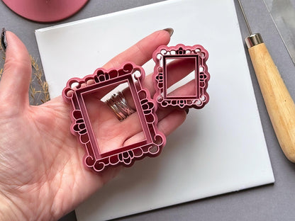 Two vintage-style rectangular frame polymer clay cutters in different sizes, held in a hand to show scale, featuring ornate decorative borders with loops, scallops and rounded accents.
