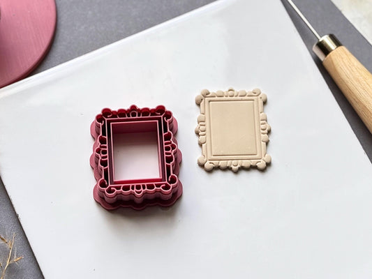 Vintage-style rectangular frame polymer clay cutter displayed beside a matching finished clay frame, featuring an ornate scalloped border with decorative boroque style loop and bead details.