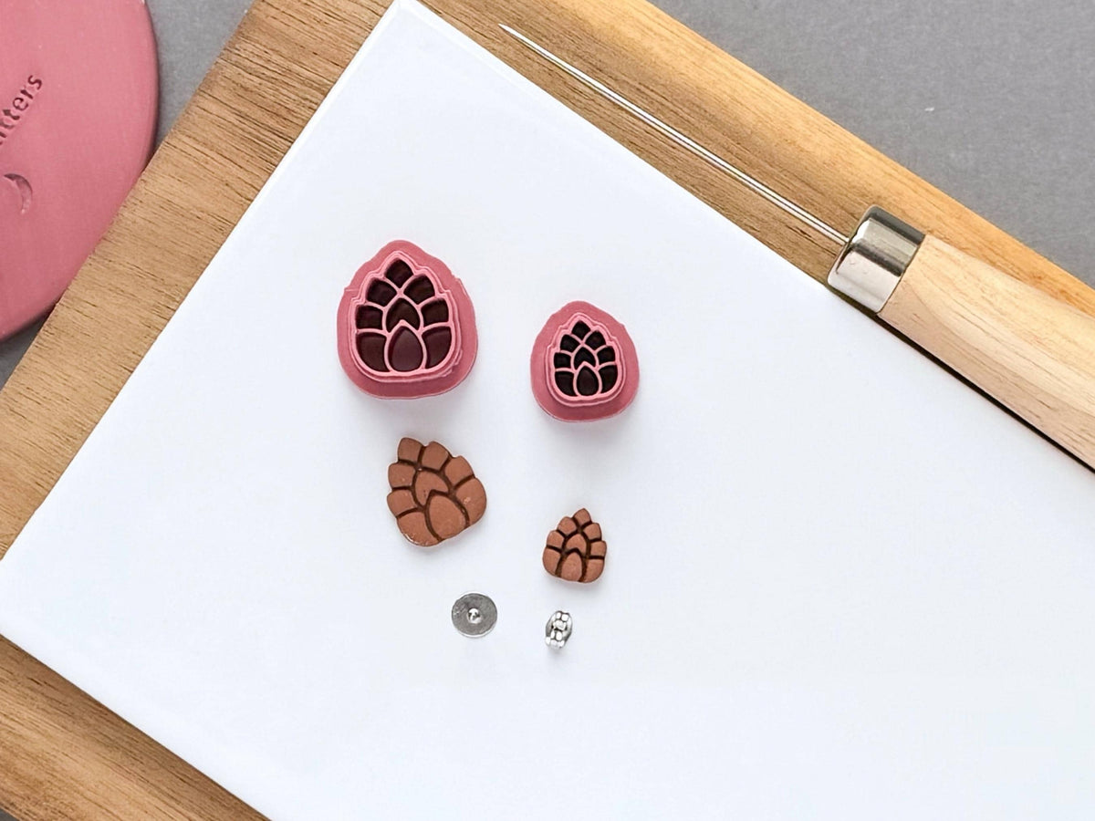 15 & 10 mm mini pink pinecone clay cutters with polymer clay cut out samples and earring posts on a white tile.
