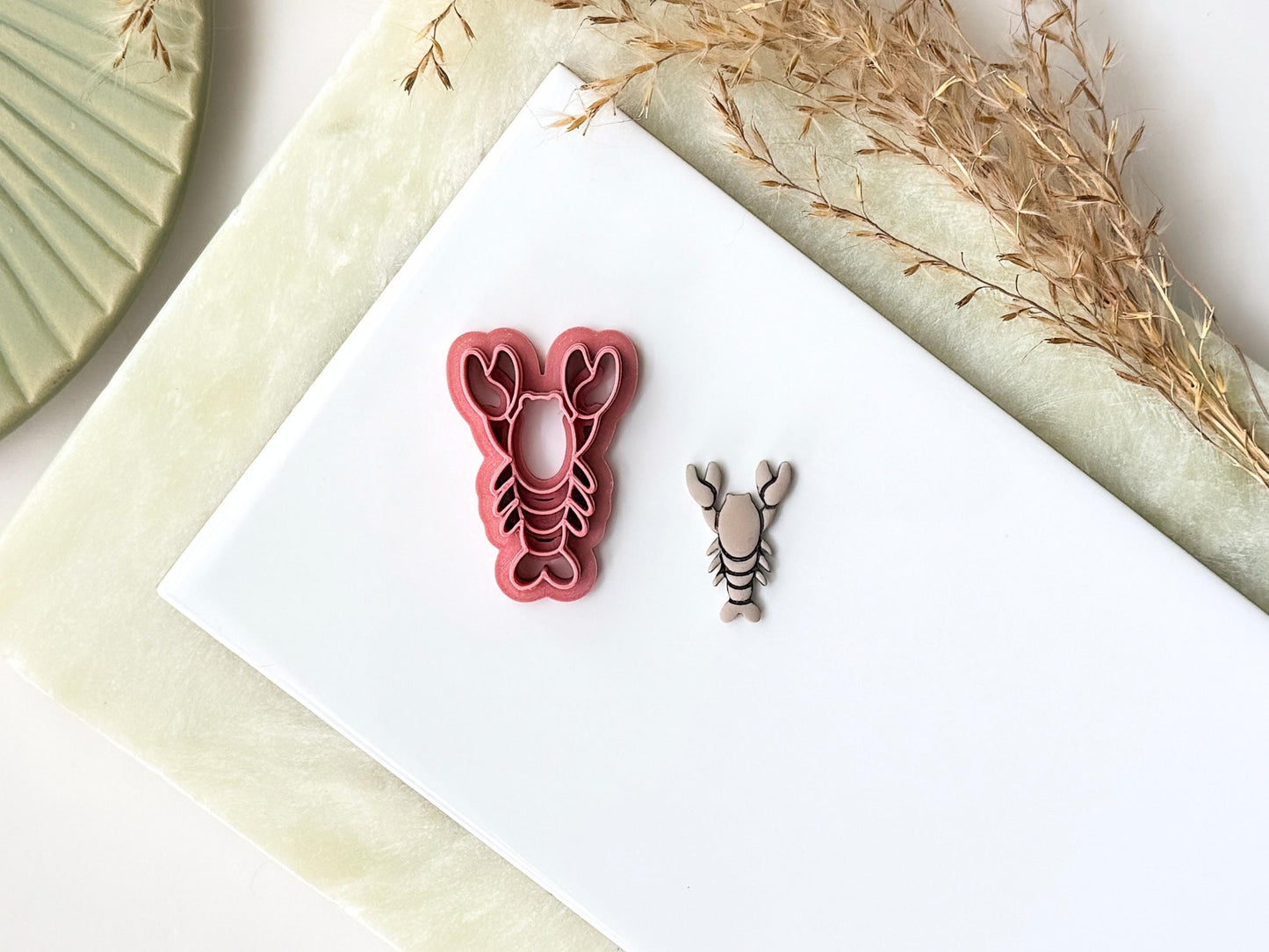 Pink lobster-shaped clay cutter with pincers and legs. Next to it is a polymer clay lobster made with the cutter.
