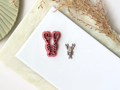 Pink lobster-shaped clay cutter with pincers and legs. Next to it is a polymer clay lobster made with the cutter.