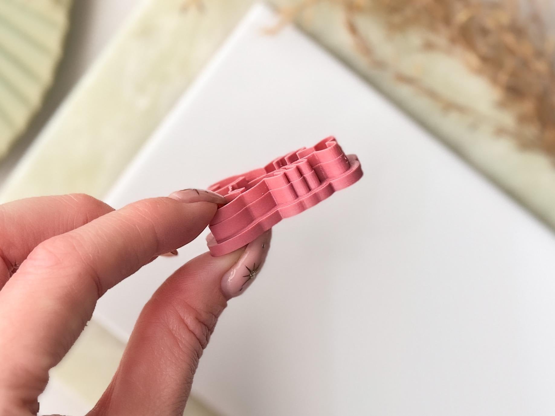 Hand holding a pink plastic ocean clay cutter against a neutral background