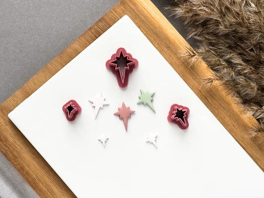 Miniature starburst polymer clay cutters displayed in three sizes on a white tile, alongside matching star shaped clay cut-outs in white, pink and sage green.