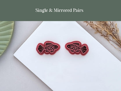 Single and mirrored pair ornamental fish polymer clay cutters displayed side by side on a white ceramic tile. The folk art-inspired fish designs are shown in left and right-facing versions for creating matching jewellery pieces.