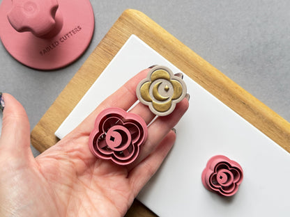 Crescent moon and star polymer clay cutter held in a hand beside a matching gold-finished clay embellishment, with a smaller flower-shaped moon cutter visible in the background.