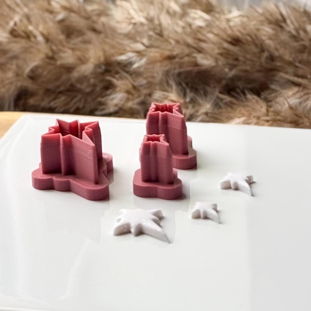 North star polymer clay cutters displayed in three graduated sizes, photographed from a low angle to showcase their raised cutting walls and deep four-point star shapes, with matching white clay cut-outs in the foreground.