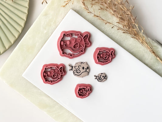 Various sizes of puffer fish polymer clay cutter on a white tile with finishe clay earrings. 
