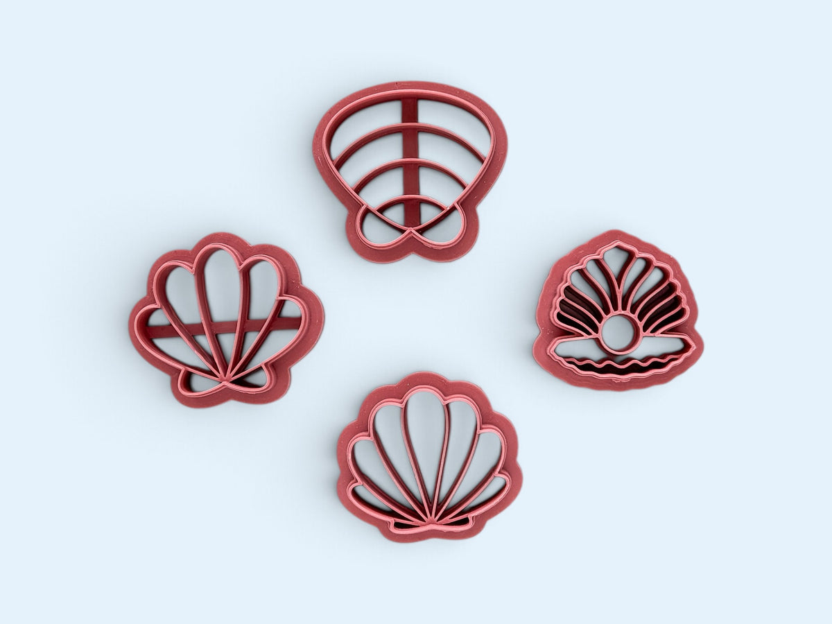 Four pink plastic seashell-shaped polymer clay cutters arranged on a light blue background.