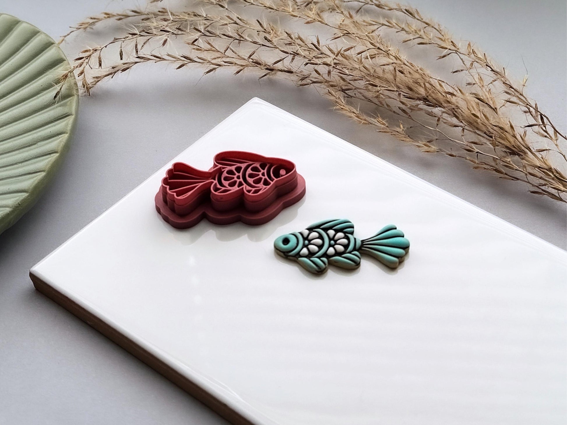 Folk art fish polymer clay cutter with detailed scale and fin designs, displayed beside a matching teal clay cut-out. UK-made clay tool for earrings, jewellery making, fondant decorating and ocean-inspired crafts.