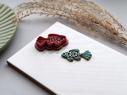 Folk art fish polymer clay cutter with detailed scale and fin designs, displayed beside a matching teal clay cut-out. UK-made clay tool for earrings, jewellery making, fondant decorating and ocean-inspired crafts.