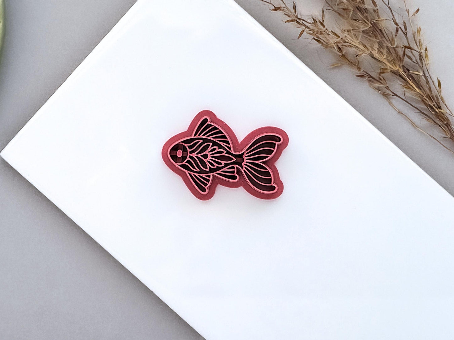 Detailed floral folk art clay cutter with fin and tail details on a white tile.