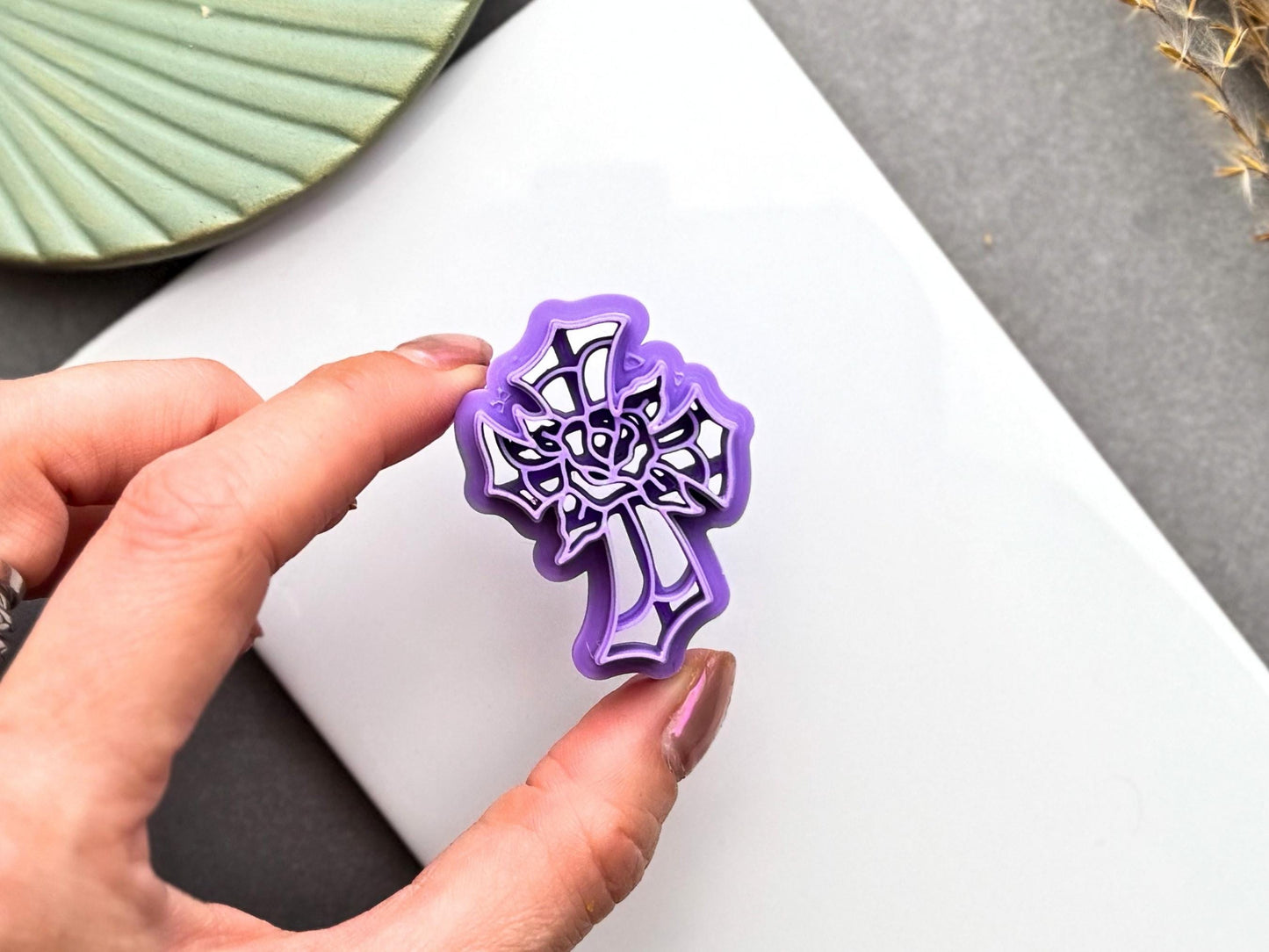 Hand holding a stained glass cross with rose polymer clay cutter for size comparison, showing the intricate floral design and cutter details.