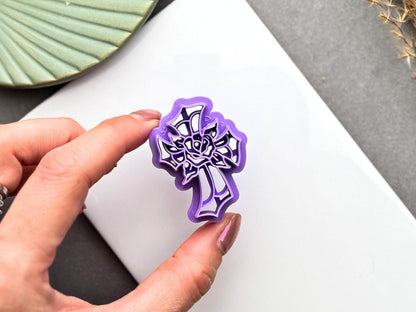 Hand holding a stained glass cross with rose polymer clay cutter for size comparison, showing the intricate floral design and cutter details.