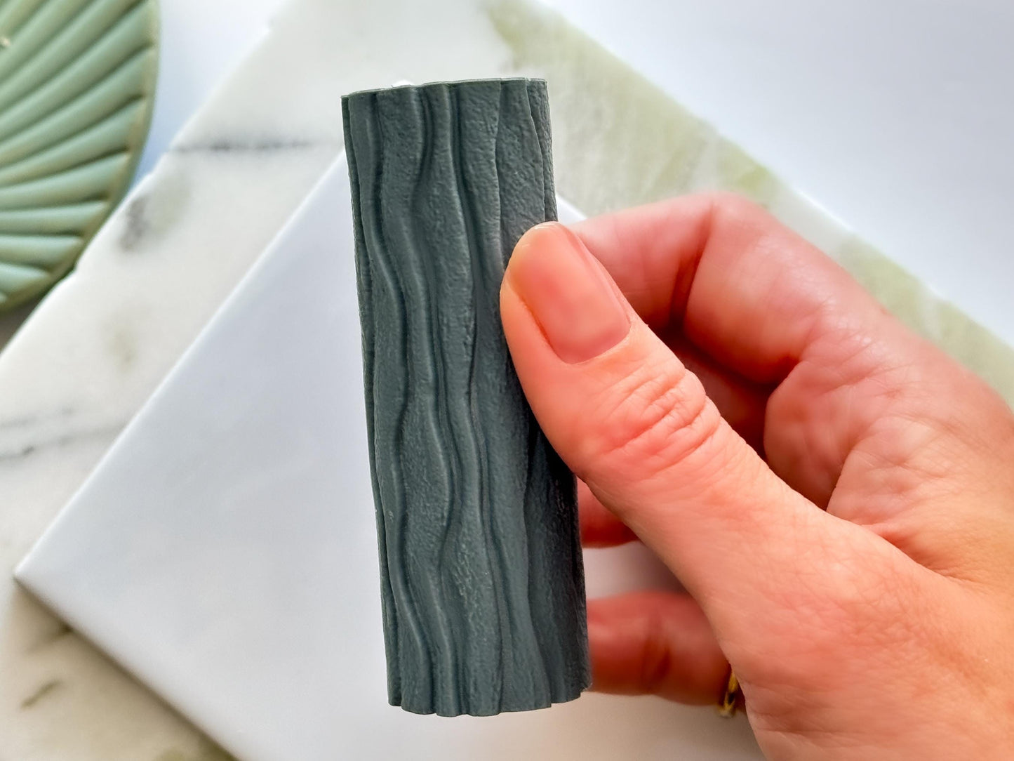 Hand holding a texture tool for polymer clay with a beach pattern in dark gray resin.