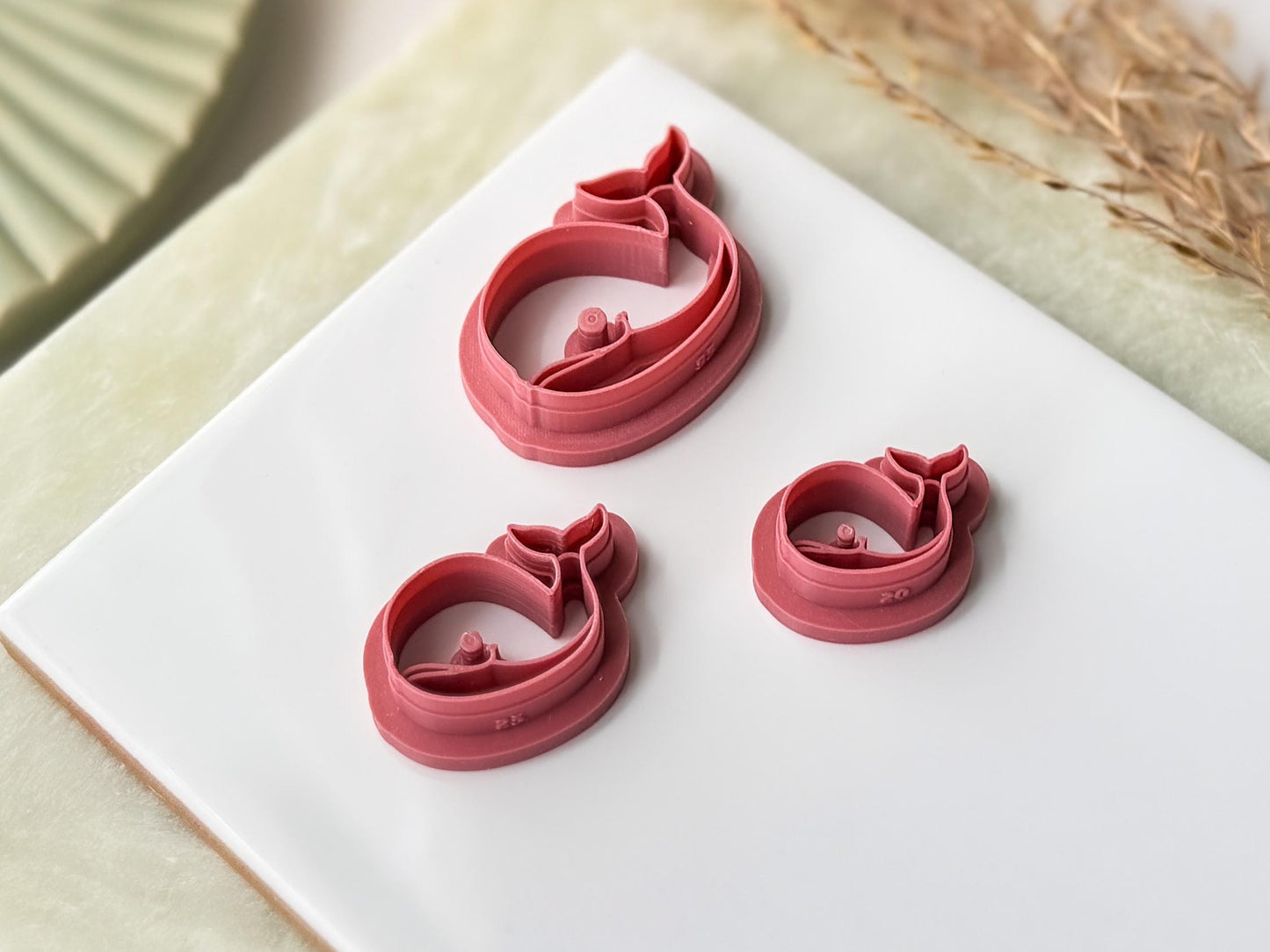 Three pibk whale shaped clay cutters in various sizes on a white surface.